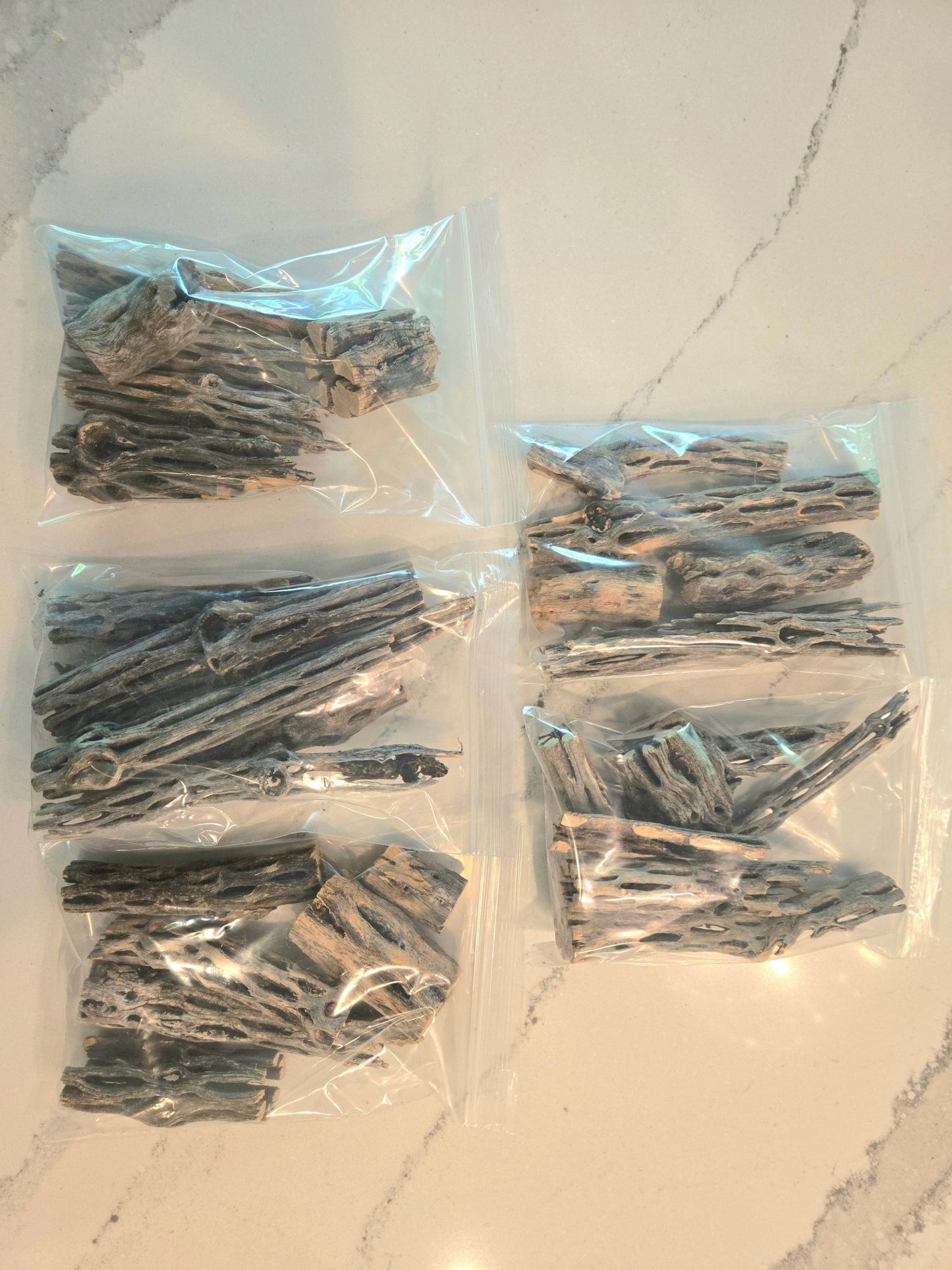 Several clear plastic bags of cholla wood displaying the weblike texture of the brown wood on a marble background.